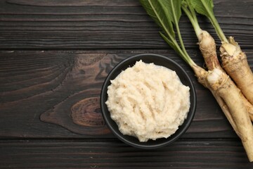 Tasty horseradish sauce and roots on black wooden table, flat lay. Space for text