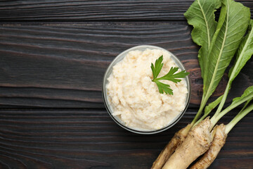 Tasty horseradish sauce with parsley and roots on black wooden table, flat lay. Space for text