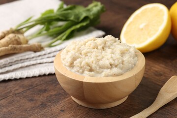 Tasty horseradish sauce and roots on wooden table, closeup