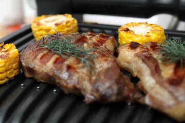 Electric grill with tasty meat, corn and dill, closeup