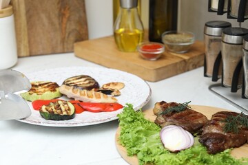 Tasty grilled meat, vegetables and spices on white table indoors, closeup