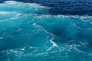 Turquoise seawater surface with foam and waves forming patterns.