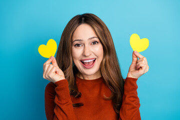 Happy woman holding yellow heart shapes while smiling against a vibrant blue background showing excitement and joy