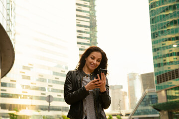 Fototapeta premium Businesswoman chatting in mobile phone in the city street high office glass buildings in sunset beautiful light 