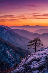 A solitary pine tree stands sentinel on a snow-covered mountaintop, framed by a vibrant sunset over layered mountain ranges.