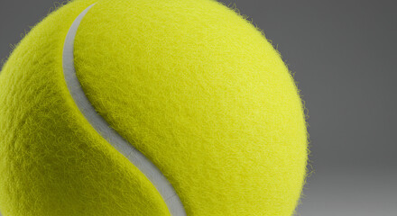 A vibrant yellow tennis ball with its characteristic white seam is captured in a close-up shot against a neutral gray background.