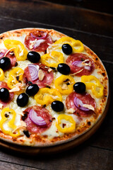 Pizza with salami, mozzarella cheese, black olives and pepper. Rustic wooden background. Soft focus. Copy space.	