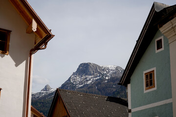 Pastel facades frame a hillside cluster of wooden cottages below a sheer rock wall. A green bracket lamp and carved balcony add crafted detail to a quaint mountain settlement in bright spring light. © VladyslavShcherbakov
