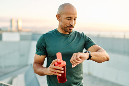 Portrait opf a young man prepering to exercise and run and looking at watch in sportwear posing for a portrait outdoors