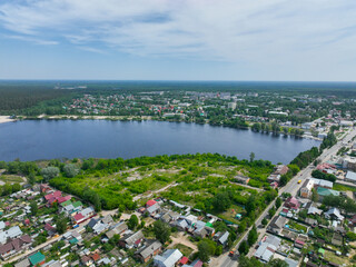 Obraz premium A wide aerial view of Gus Khrustalny, showing residential houses along the shore of a large lake with green fields and a dense forest on the horizon.