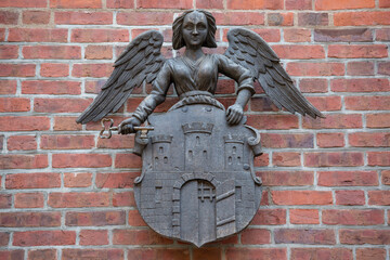 Angel holding coat of arms of city of Toruń, metal sculpture above gate of Old Town Hall, Torun, Poland