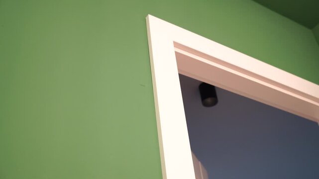 A small, discreet security camera installed in the corner of a white door frame against a green wall, symbolizing modern home surveillance, safety, and privacy concerns