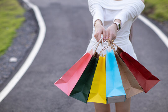 A young Asian woman holds several colorful shopping bags in her hands after going shopping in a shopping mall because of a holiday sale. Many colorful shopping paper bags in the hands of a young woman