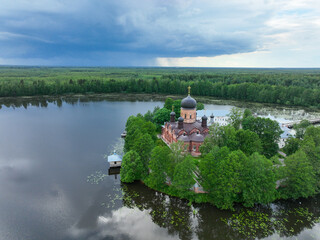 Obraz premium An aerial view of the Vvedensky Island Monastery with its black domes and red walls, located on a small, tree-covered island in a wide lake.