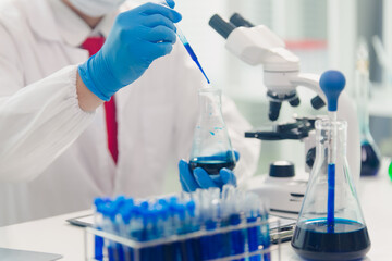 Fototapeta premium medical or scientific researcher researching and experimenting Multi-colored solution, vial and microscope In the laboratory or in the laboratory by wearing blue gloves and white clothing completely.