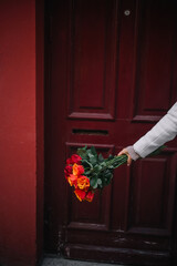 Hand holding a vibrant bouquet of roses in front of a red door