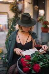 Woman enjoying a glass of red wine while reading at a quaint outdoor cafe in the evening