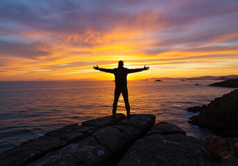 Man celebrating freedom with arms open wide during stunning sunset over ocean and horizon