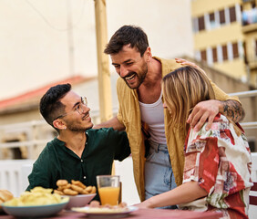 Happy young people having fun during a rooftop party during a summer holiday, sitting by the table talking, eating and drinking, love, romance, relationship, flirting and youth culture concept