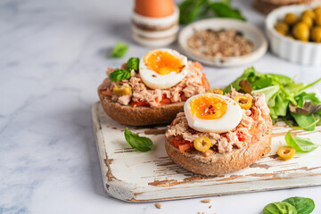 Tuna toast. Open sandwiches with whole grain bread, canned tuna, boiled egg, tomatoes and olives on white background. Healthy breakfast food