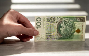 Hand holding 100 Polish złoty banknote – close-up currency concept symbolizing money, savings, finance, income, investment, and economic value in Poland