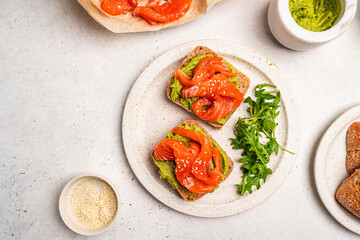Avocado salmon sandwich or toast on rye bread with guacamole sauce, arugula and sesame seeds, white background, top view. Healthy food concept.