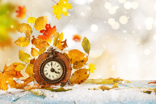 Alarm clock and autumn leaves on table outdoors. Daylight saving time end