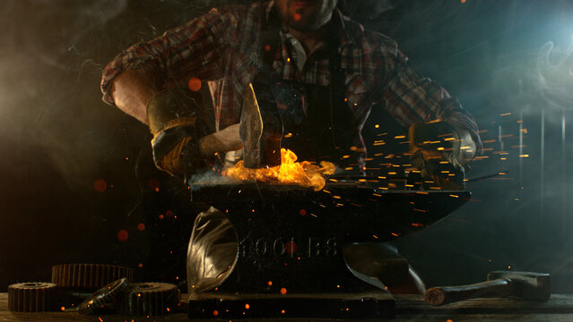 Close-up of blacksmith forging glowing hot iron on anvil with flying sparks
