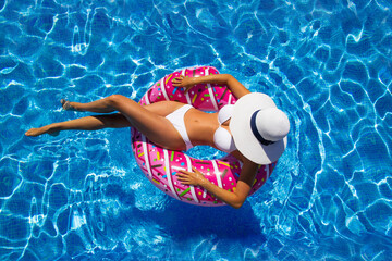 Beautiful brunette woman sits on an pink inflatable ring at swimming pool