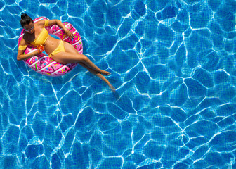 Beautiful brunette woman sits on an pink inflatable ring at swimming pool