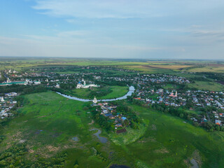 Fototapeta premium A wide aerial view of the city of Suzdal, showing the Kamenka River winding through the urban area and two historical monasteries.