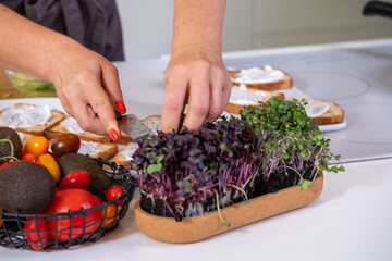 Female chef preparing fresh microgreens and vegetables on a kitchen countertop, showcasing vibrant colors and healthy ingredients for culinary creativity and meal preparation