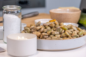 Fresh fava beans in a modern kitchen setting, arranged in a stylish bowl alongside salt, cream, and other ingredients, showcasing culinary preparation and vibrant colours