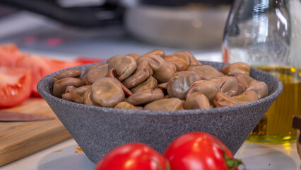Bowl filled with fresh brown beans surrounded by ripe tomatoes and olive oil on a kitchen countertop, showcasing vibrant ingredients for healthy cooking with banner