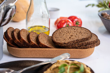 Freshly baked dark full grain bread slices arranged on a natural cork tray with olive oil and tomatoes, showcasing healthy nourishment and copy space for text
