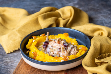 Fresh pumpkin puree served in a bowl with chicken and nuts, garnished with cranberries, surrounded...