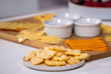 Fresh organic crackers and cheese slices arranged on a wooden board with bowls of dip, showcasing a healthy snack concept for nutrition enthusiasts and culinary creativity