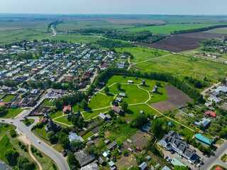 A wide aerial shot of the city of Suzdal, showing a mix of modern houses and the wooden architecture museum with windmills on a large green field.