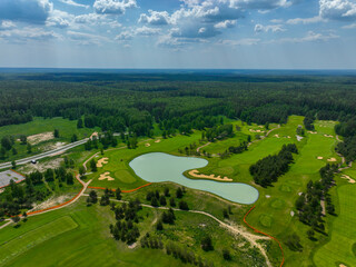 A wide aerial view of a beautiful golf course with a large, central lake and sand bunkers, with a dense forest stretching to the horizon.