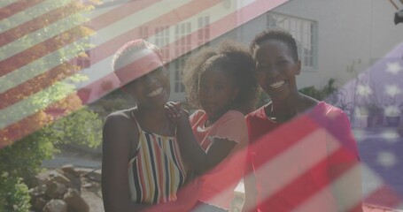 Smiling three generations embracing in sunlit front yard, with American flag overlay