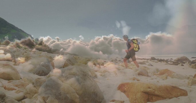 Traversing hiker carrying yellow backpack on boulders, sand near hillside with rainbow, copy space - Powered by Adobe