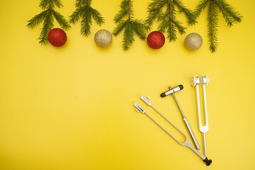 Christmas Medical Instruments with Christmas Tree and red and gold balls on yellow Background. New Year's photo of a medical hammer, orchidometer, tuning fork, stethoscope