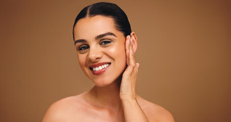 Portrait, makeup and touch face of female model on brown background for cosmetics and coverage. Skin glow, foundation and confidence of woman in studio with mockup, space and smile for facial