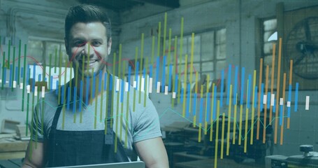 Smiling craftsman wearing apron holding laptop in woodshop, with planks, tools and data overlay