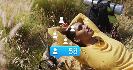 Reclining hiker in yellow top on rock in meadow, with backpack, hiking poles, notification bubble