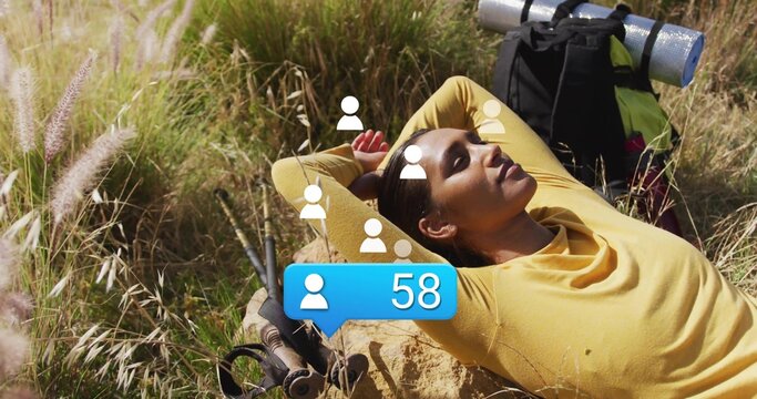 Reclining hiker in yellow top on rock in meadow, with backpack, hiking poles, notification bubble - Powered by Adobe