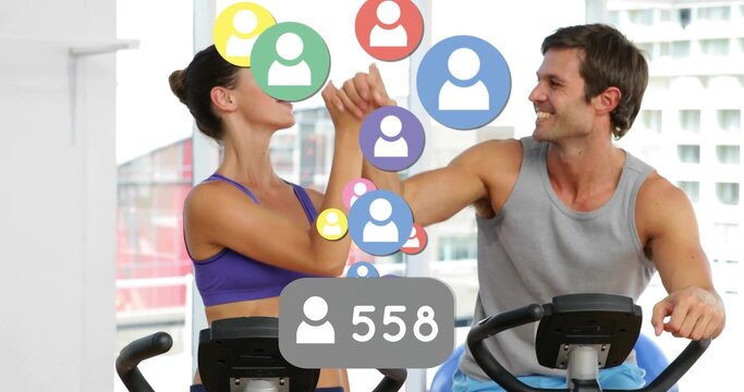 Pedaling pair in sportswear on stationary bikes in gym with social media icons and 558 badge - Powered by Adobe