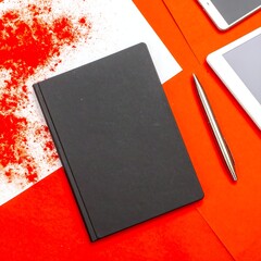 Flat lay of black notebook, red paper, and digital devices