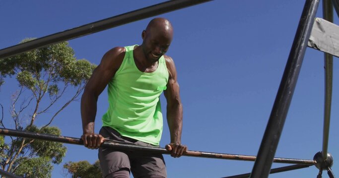Lifting man wearing sleeveless green shirt pulling upward on metal fitness bars at park - Powered by Adobe