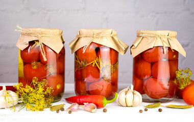Glass jars with homemade pickled tomatoes preserved with garlic, dill, and spices. Organic farm vegetables in marinade. Close-up.